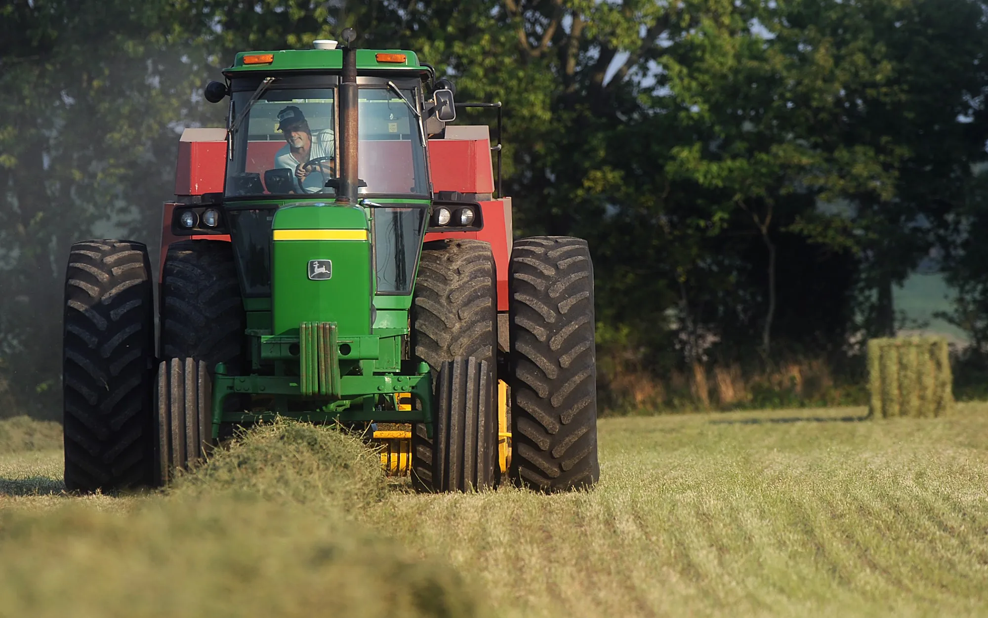 A farmer baling hay on a green tractor in a cut field